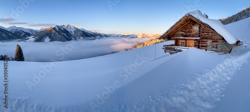 Snow covered mountain hut old farmhouse in the Austrian alps at sunrise against blue sky.