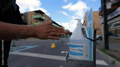 Selective focus of young man hands using dispenser to apply alcohol based sanitizer for safety against covid-19 on downtown street photo