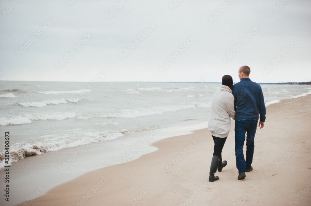 Couple hugging and walking on sandy beach on cold windy winter day Couple hugging and walking on sandy beach on cold windy winter day