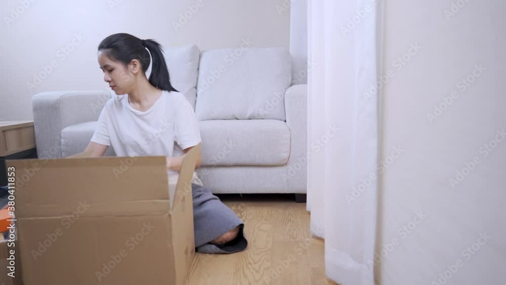 shot of young putting things into the parcel carton box, preparing to move out, sit down couch on the background, Multitasking works house arranging, budget Relocating financial crisis, stay at home shot of young putting things into the parcel carton box, preparing to move out, sit down couch on the background, Multitasking works house arranging, budget Relocating financial crisis, stay at home