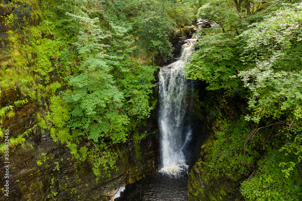 Aerial drone view of a tall waterfall in a narrow canyon surrounded by trees (Sgwd Einion Gam, Wales, UK)