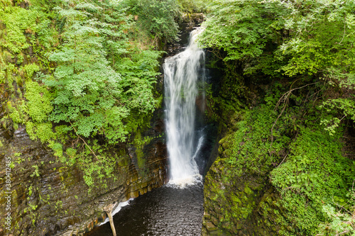 Aerial drone view of a tall waterfall in a narrow canyon surrounded by trees  Sgwd Einion Gam  Wales  UK 