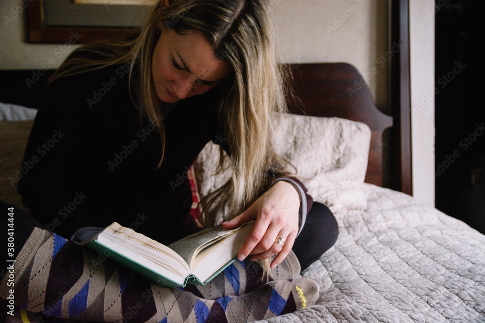 Blonde woman sitting on a bed reading a book Blonde woman sitting on a bed reading a book
