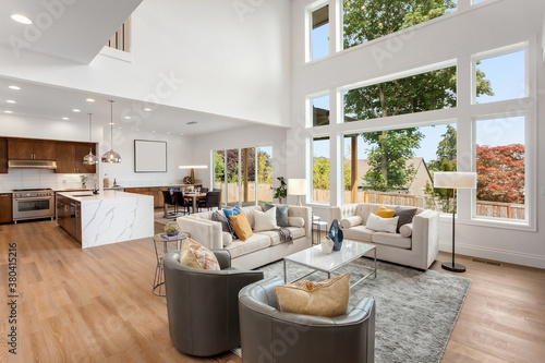 Beautiful living room and kitchen interior in new modern luxury home with large bank of windows showing exterior view. Features open concept floor plan, waterfall island, stainless steel appliances
