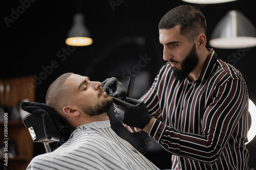 stylish mens beard trim at the barbershop, short trendy hair brown hair Caucasian appearance. Beard and mustache on the face. Dark trendy up-to-date Barber shop interior
