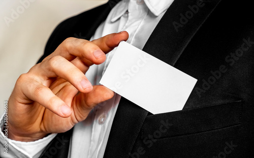 Part of body of man who takes out business card from the pocket of business suit, copyspace. Businessman in black business suit puts white card in pocket. Business concept.