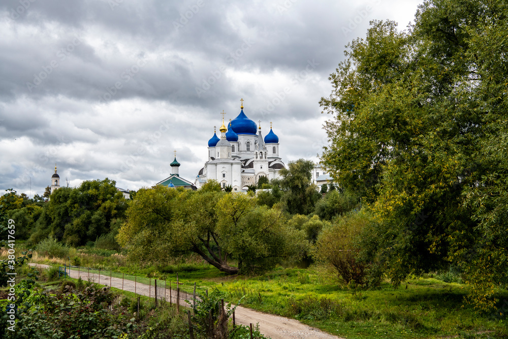 old white monastery with blue domes on the background of green trees and the river old white monastery with blue domes on the background of green trees and the river