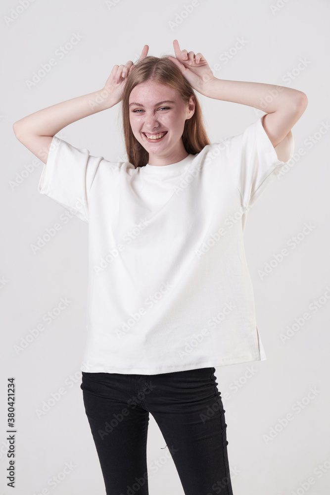 Playful teen blond girl shows horns in the studio on white background. Human emotions, facial expression concept Playful teen blond girl shows horns in the studio on white background. Human emotions, facial expression concept