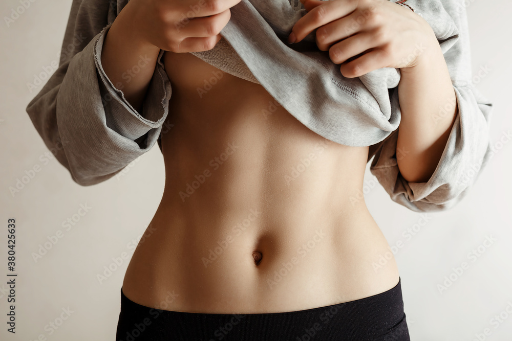 girl shows her pumped belly press by a sweater - obrazy, fototapety, plakaty 