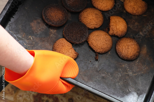 Burnt cookies. A hand in  orange oven glove, potholder picks up a black baking tray with burnt cookies photo