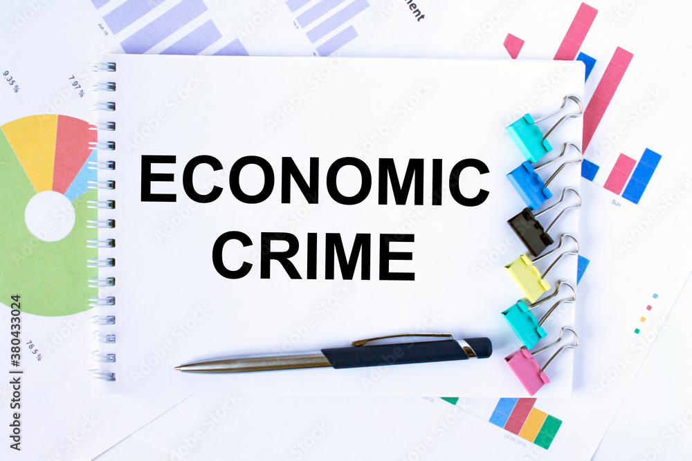 Notepad with text Economic Crime, paper clips, blue pen on financial diagrams Notepad with text Economic Crime, paper clips, blue pen on financial diagrams