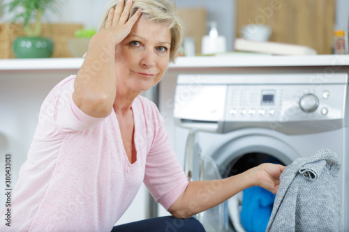 forgetful mature woman by washing machine holding jumper