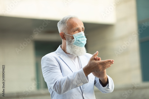 Coronavirus bearded senior man wearing face mask using antiseptic bottle dispenser hand sanitizer alcohol gel hand wash. Covid-19.