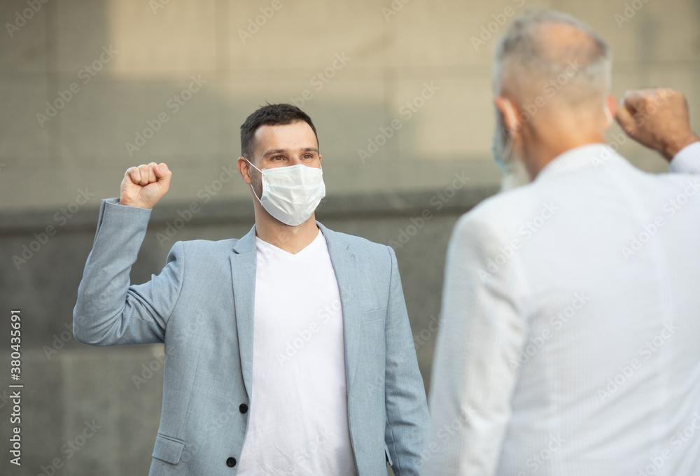 Two friends wearing face masks meeting and standing against the wall in outdoors for social distancing for infection risk and disease prevention COVID-19.