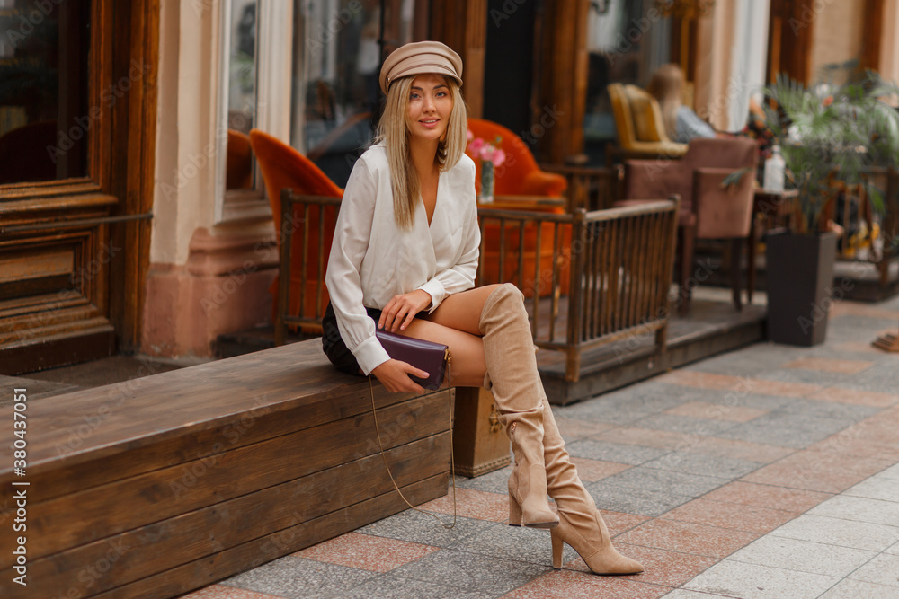 Good looking sexy blond model in white blouse and leather skrt and knitted  block thigh high boots in beige. Sitting on bench on the street. Full  lenght. Stock-Foto | Adobe Stock