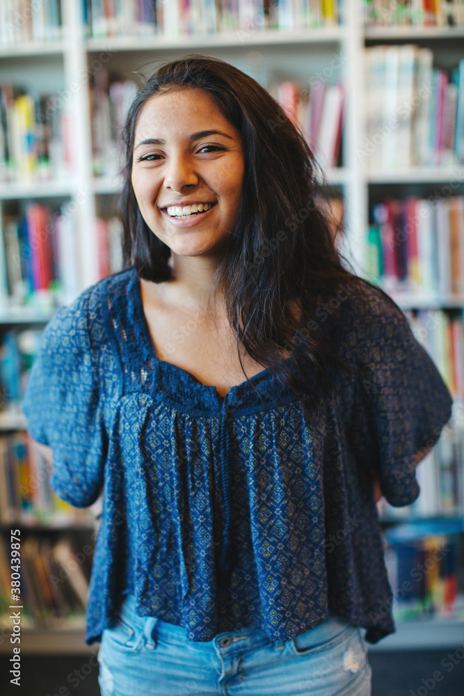 Portrait of happy high school teenage girl holding book binder in library