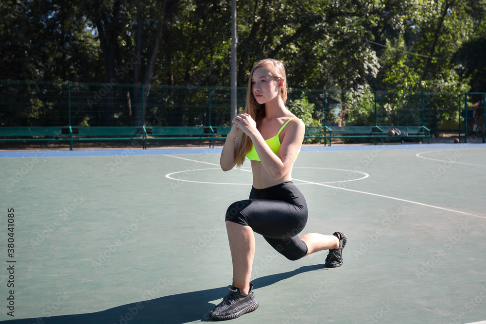 Fototapeta premium Young attractive girl in sportswear doing lunge exercise on the sports ground