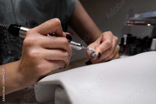 Hardware manicure at home. Woman is applying electric nail file drill on her fingers. Mechanical manicure close-up. Body care concept.