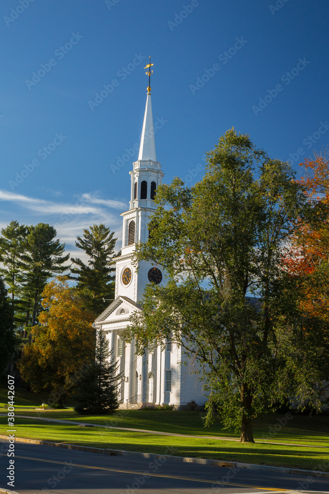 Fototapeta premium A traditional American White Church with high Steeple. Trees are showing autumn fall colors. Williamstown, MA