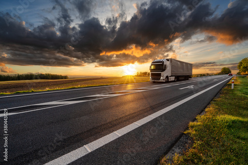 Truck driving on the asphalt road in rural landscape at sunset with dark cloud