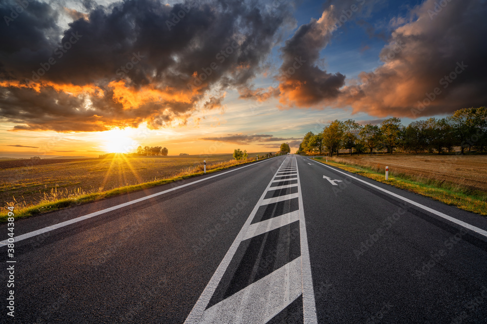 Empty asphalt road in rural landscape at sunset with dark cloud