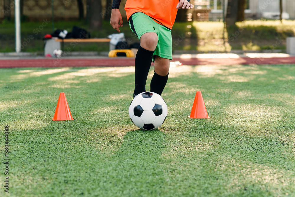 Persistent teen soccer player kicking ball on field. Close up feet of footballer kicking ball on green grass. Persistent teen soccer player kicking ball on field. Close up feet of footballer kicking ball on green grass.