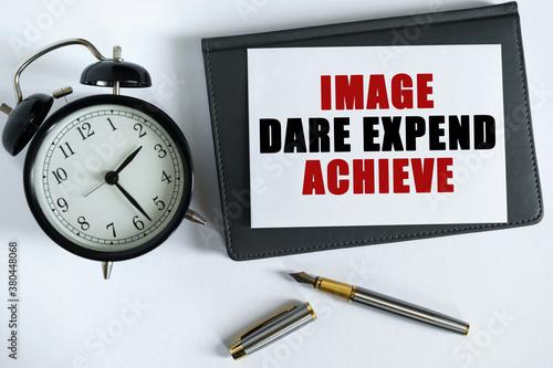 On the table there is a clock, a pen, a notebook and a card on which the text is written - IMAGE DARE EXPEND ACHIEVE.