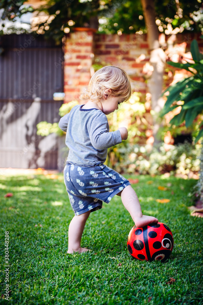 Small boy kicking a red ball outside in a yard Small boy kicking a red ball outside in a yard