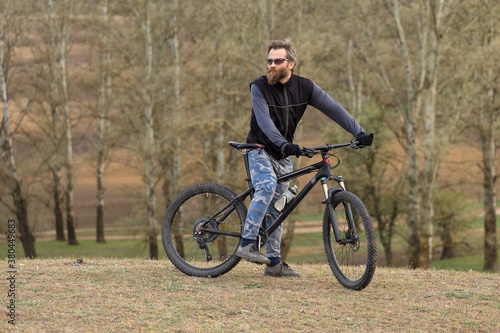 Sports brutal bearded guy on a modern mountain bike. Cyclist on the green hills in the spring. © Mountains Hunter