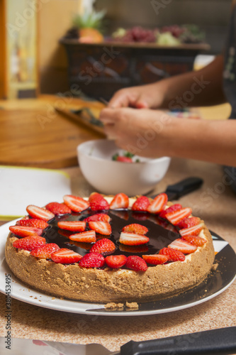 selective focus of a delicious cheesecake with strawberries and blurred female hands cutting fruits