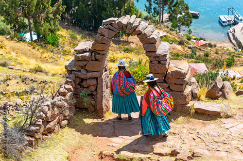 Bild auf Leinwand Two peruvian indigenous Quechua women in traditional clothing under an arch walking down steps to a harbor, Taquile island, Titicaca Lake, Peru