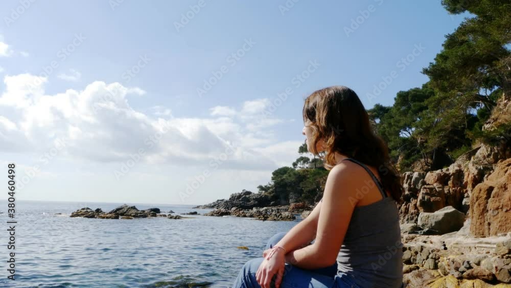 A teenage girl admires the Mediterranean sea on a rocky seashore, 4k A teenage girl admires the Mediterranean sea on a rocky seashore, 4k