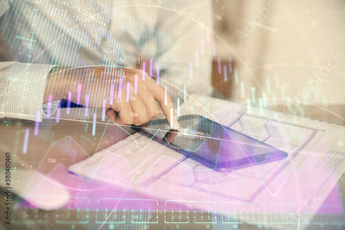 Double exposure of man's hands holding and using a digital device and forex graph drawing. Financial market concept.