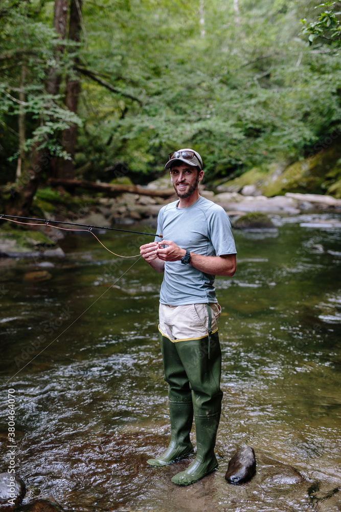 Man smiling and fly-fishing in clear river trying to catch fish Man smiling and fly-fishing in clear river trying to catch fish