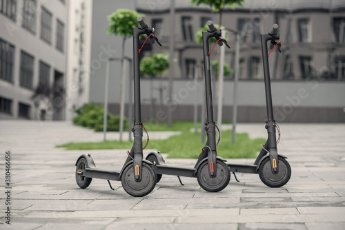 Three modern stylish black electric scooter are parked near big office centre. Electricity and eco friendly concept.