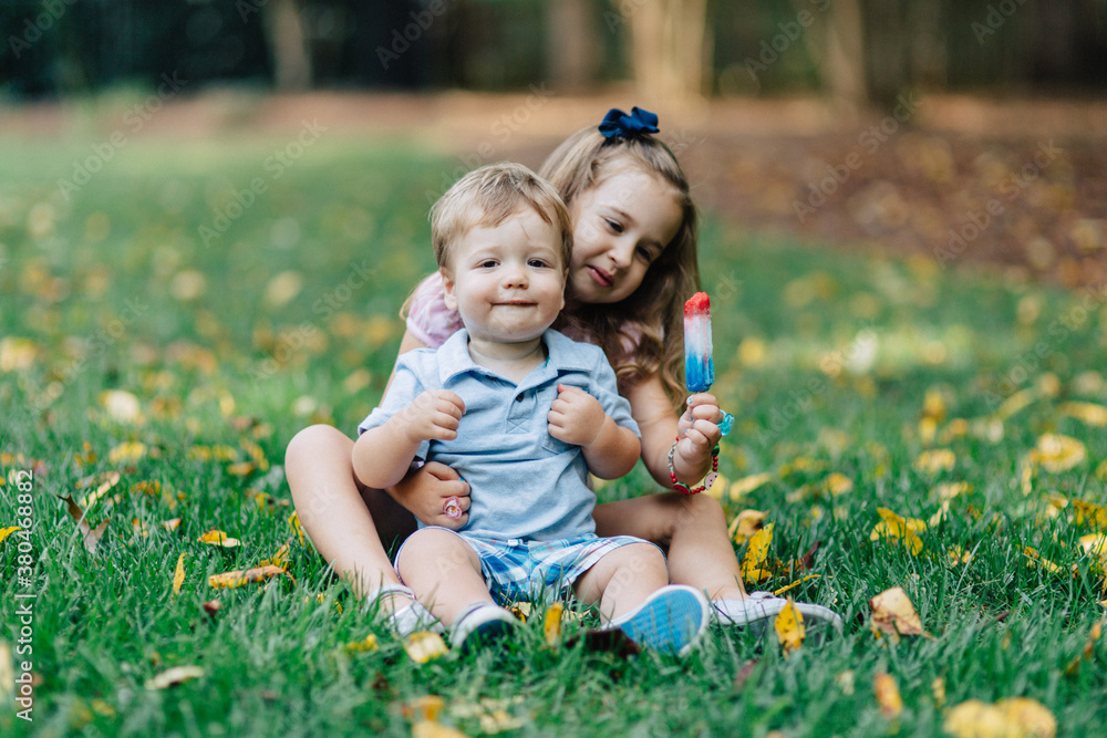 Sister and brother sitting in grass sharing a popsicle Sister and brother sitting in grass sharing a popsicle