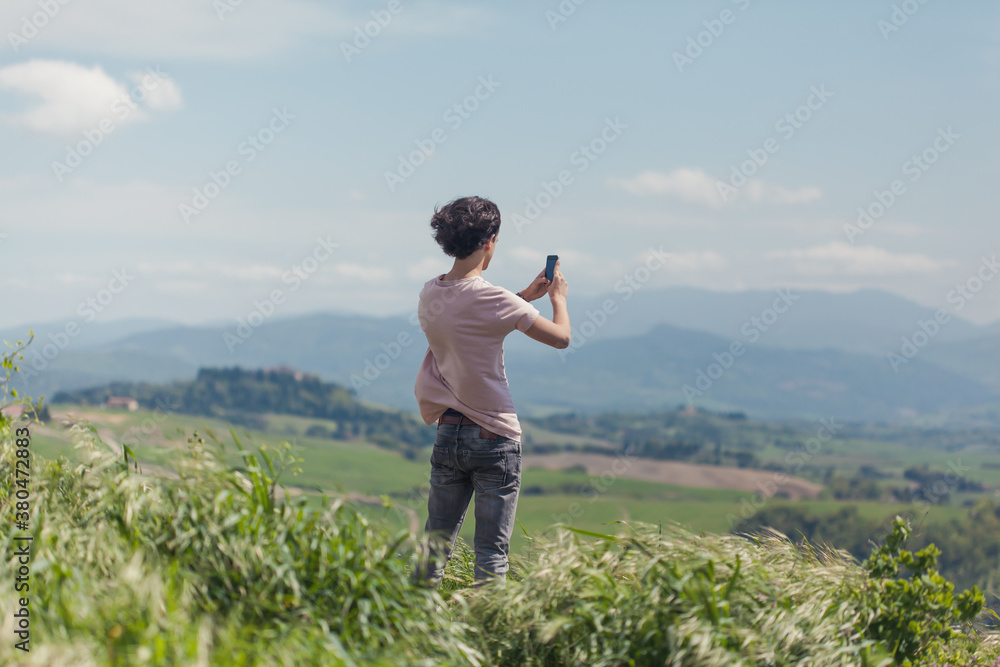 Teenage boy standing in the hills in Tuscany taking a picture with his phone Teenage boy standing in the hills in Tuscany taking a picture with his phone