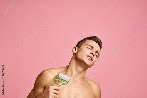 Handsome man with massager in hand on isolated pink background cropped view clean skin