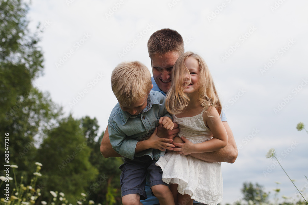 A father playfully picks up his son and daughter A father playfully picks up his son and daughter