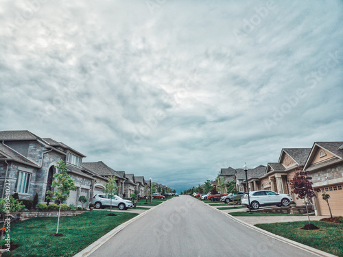 Gloomy weather with dramatic sky clouds in Alliston town, Ontario, Canada. Landscape scene with residential area road street and front yards of houses. Grey blue cloudy day outdoors.