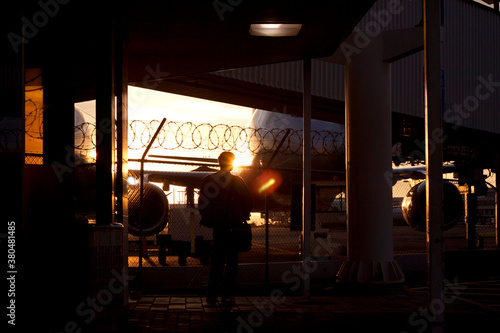 A person standing looking at a plane at the airport during sunset.