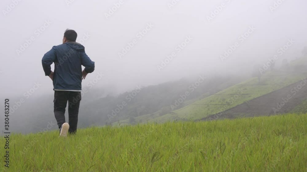 4K Asian man tourist in blue jacket pulling the hood over head and walking against strong wind on mountain. Male hiker hiking on the hill in foggy day. Outdoor lifestyle and bad weather travel concept 4K Asian man tourist in blue jacket pulling the hood over head and walking against strong wind on mountain. Male hiker hiking on the hill in foggy day. Outdoor lifestyle and bad weather travel concept