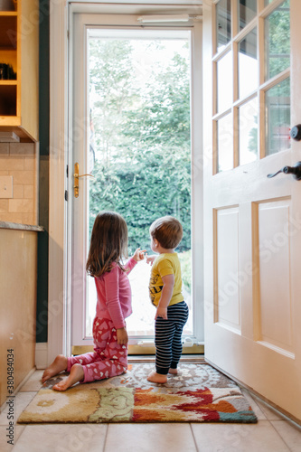 Two children and a dog looking outside through a glass door photo