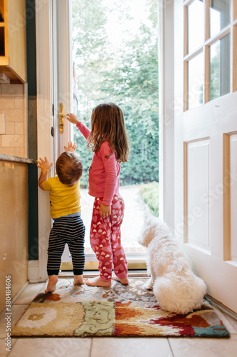 Sister helping little brother opening a door with dog watching photo