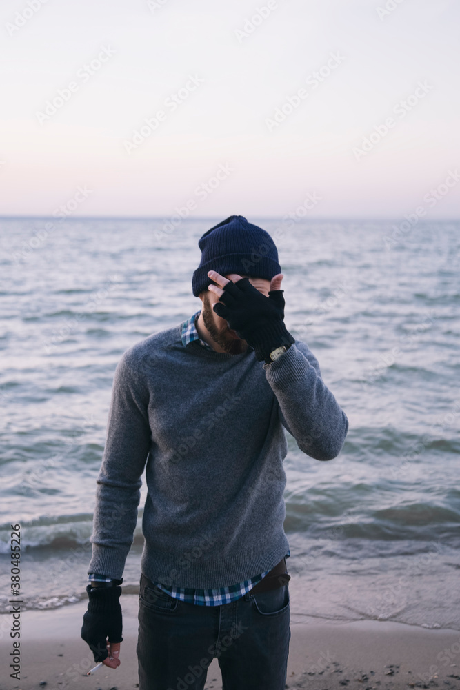 Bearded man standing near the sea, covering his face with hand Bearded man standing near the sea, covering his face with hand