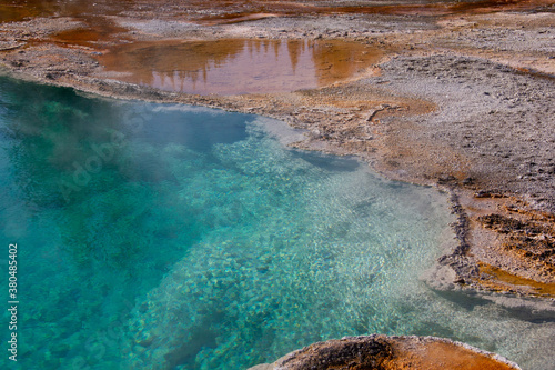 West Thubb Geyser Hotspring. Deep light blue hot spring. Color contrast abstract background. Sandy yellowish brown. Blue water. Reflecting tree