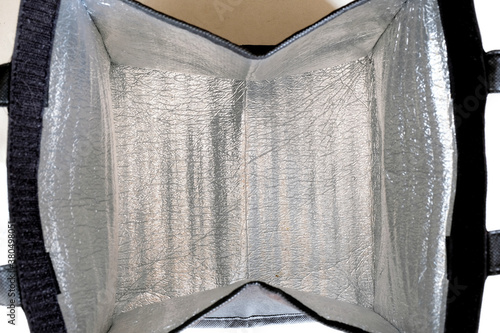 Inside of an opened foldable insulated thermal bag, showing the padded silver aluminum foil or insulating material to keep meals warm or cold, conveniently use for delivery or transporting food.