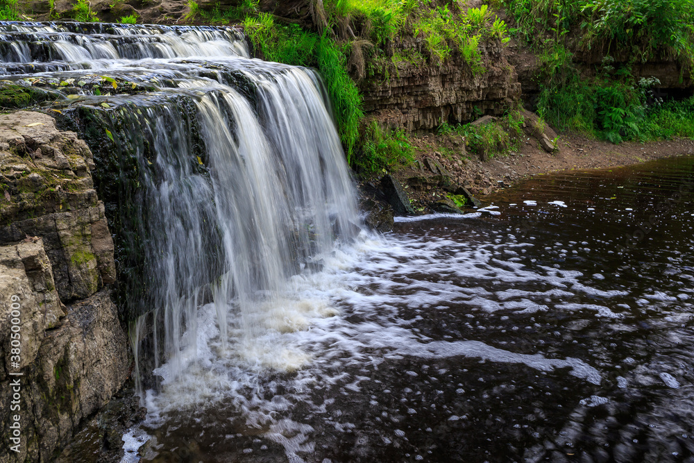 Beautiful waterfall closeup. A small forest river. Streams of water fall from the rock. Sablino waterfall, canyon of Sablinka River, Leningrad Region, Russia.