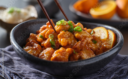 eating bowl of chinese orange chicken with chopsticks