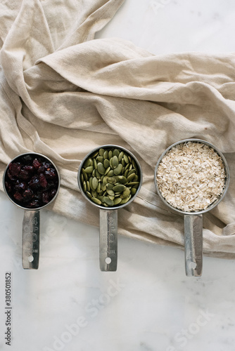 Homemade grandola nuts and oats ingredients in measuring cups on marble table photo